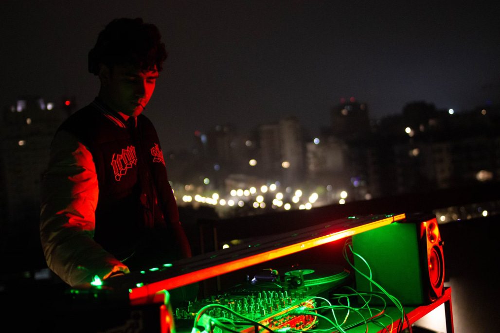 Set en terraza con controladora iluminada y el skyline nocturno de la ciudad detrás.
