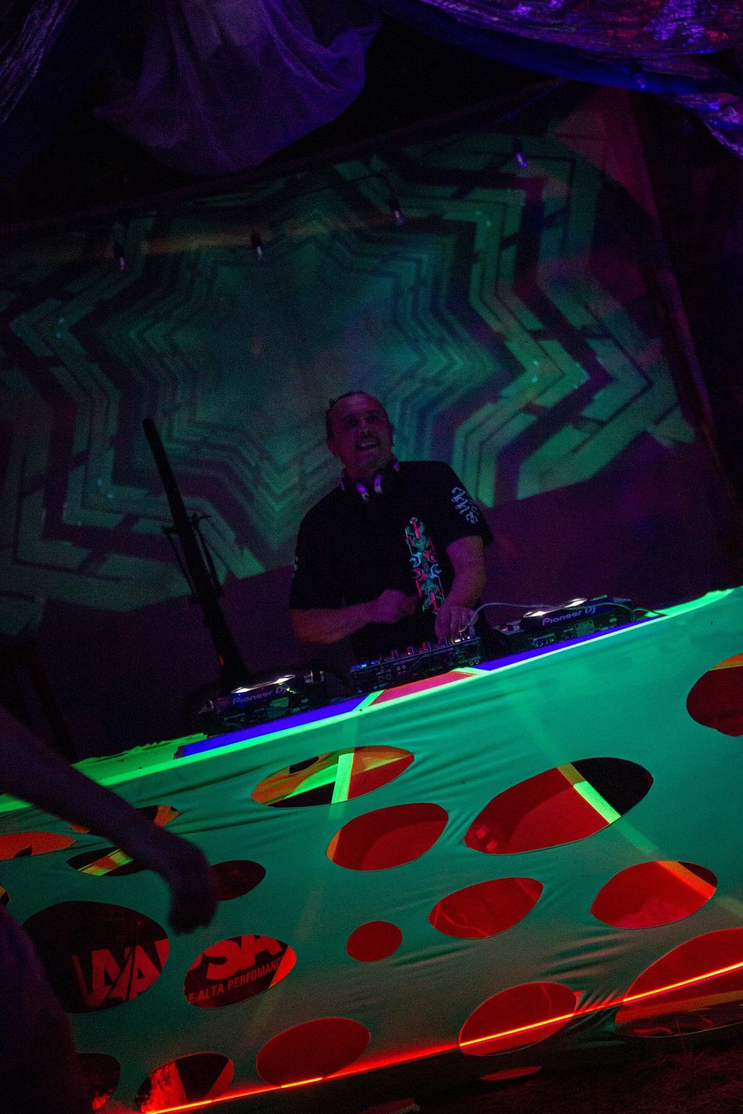 Cabina montada bajo telas reactivas a UV en verde y rojo, con público alrededor.
